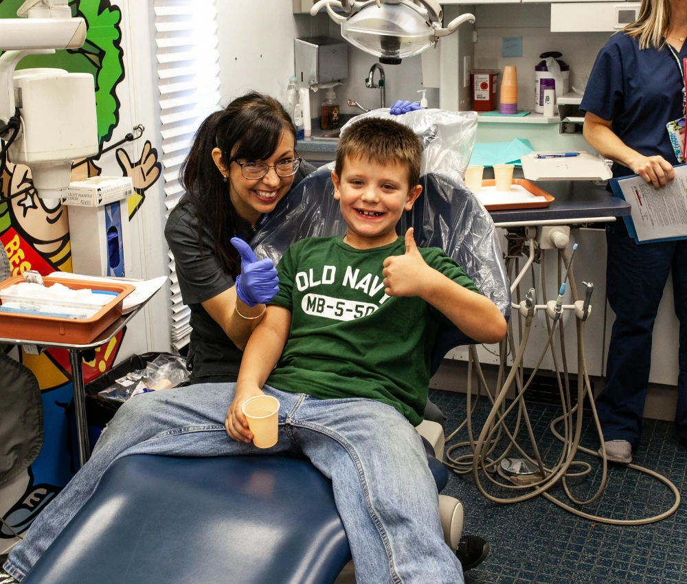 dentist and young patient both smiling and giving a thumbs up after receiving dental care