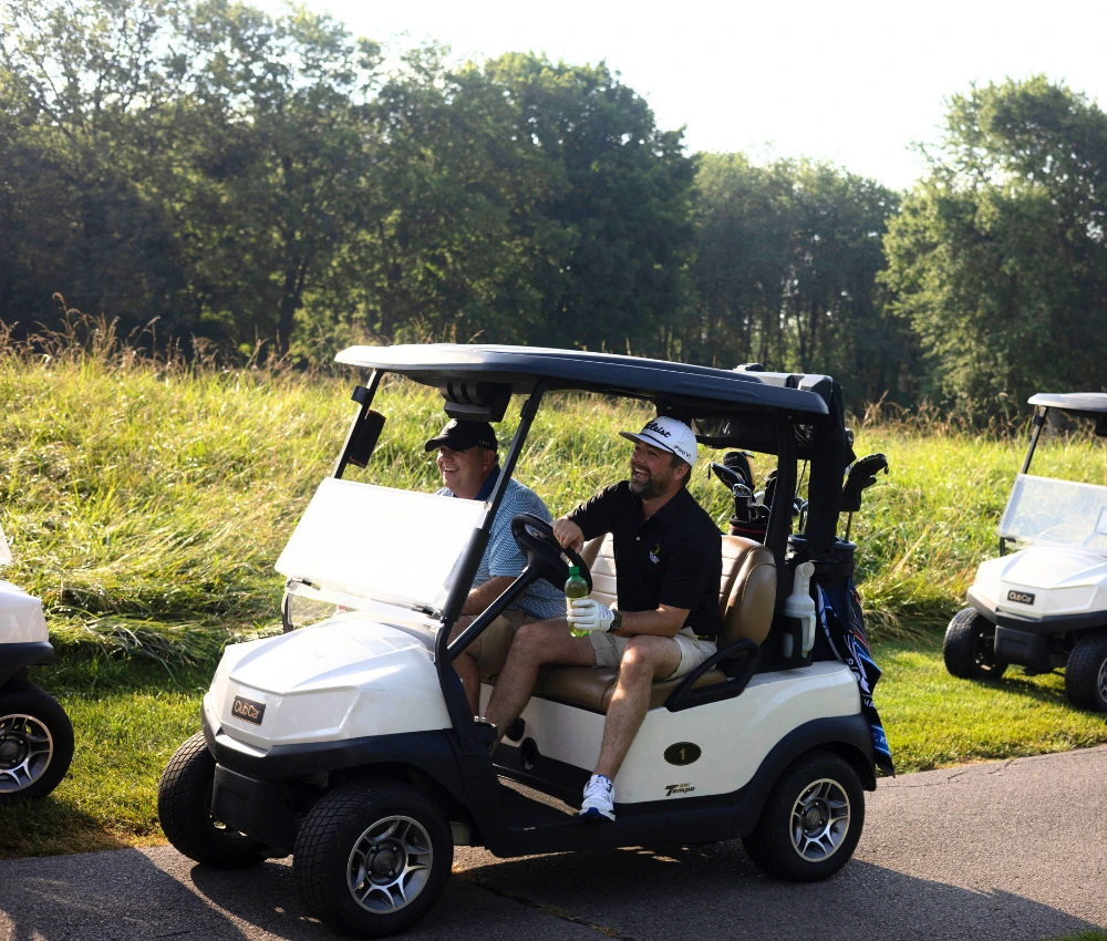 two golfers smiling as they ride around in a golf cart