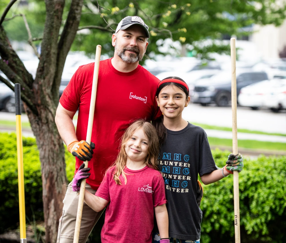 volunteer with two children smiling as they perform yard cleanup duties